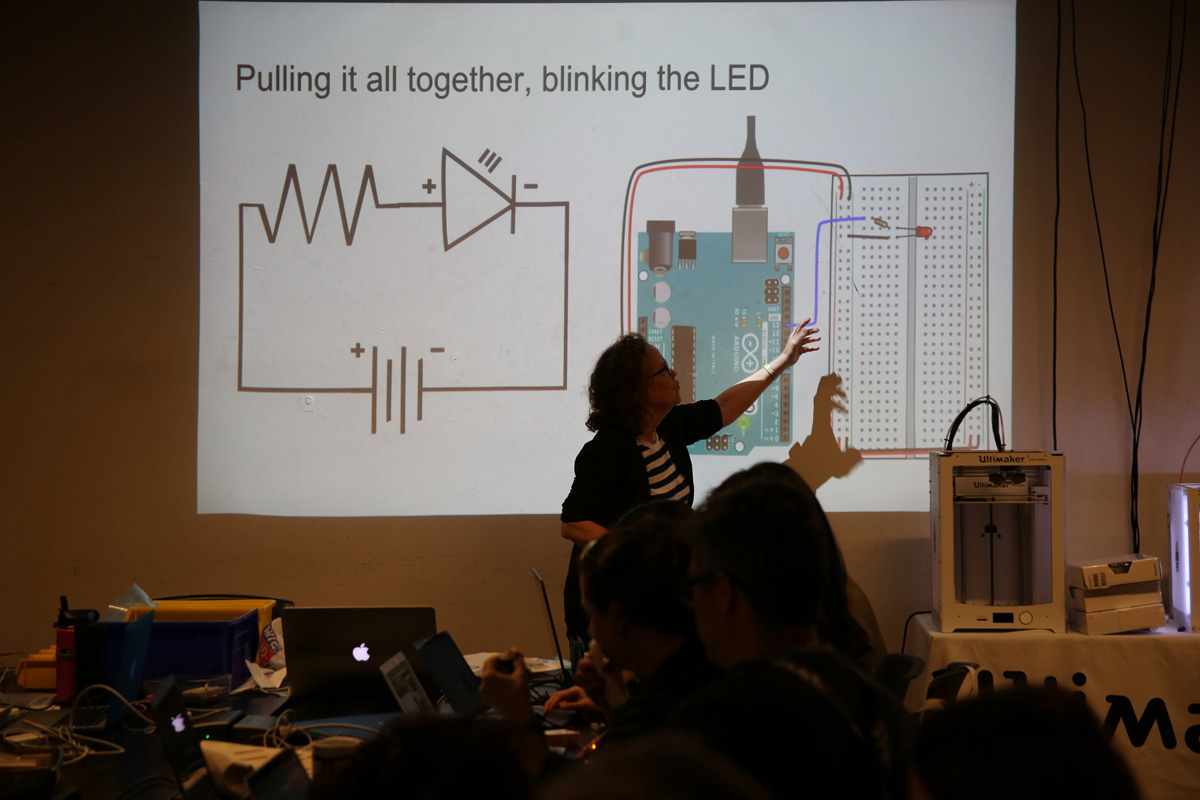 a woman giving a lecture and pointing to a projection of an Arduino and LED